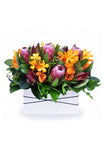 tropical blooms such as Mokara orchids and Proteas arranged in a ceramic vase